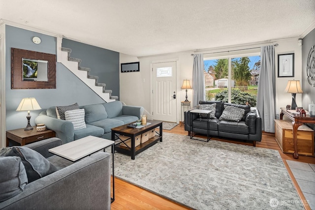 living room featuring stairs, light wood-type flooring, and a textured ceiling