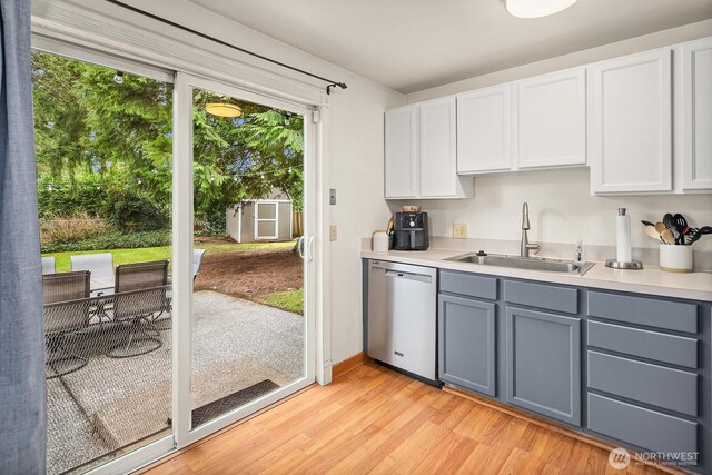 kitchen with gray cabinetry, dishwasher, light wood-type flooring, light countertops, and a sink