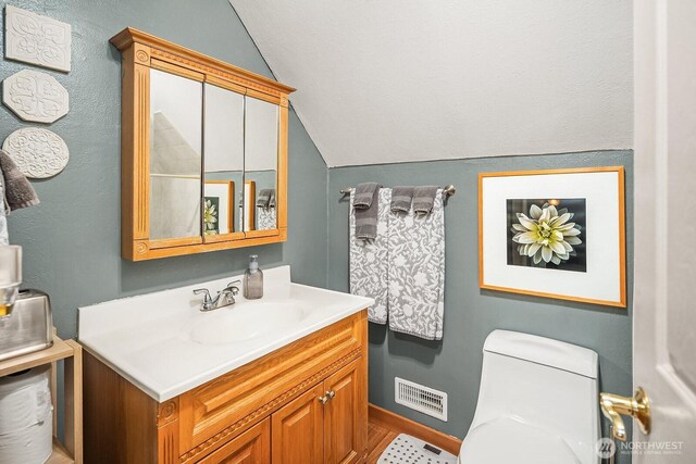 bathroom featuring visible vents, toilet, vanity, and vaulted ceiling