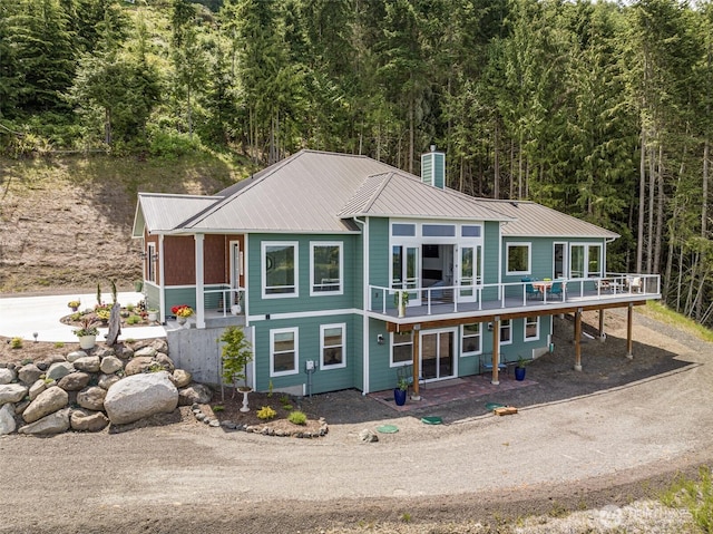 view of front of house with a forest view, driveway, a wooden deck, a chimney, and metal roof