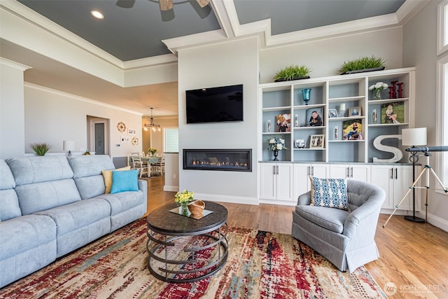 living area featuring a ceiling fan, baseboards, light wood-style flooring, ornamental molding, and a glass covered fireplace