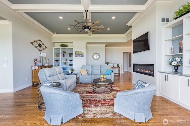 living room featuring a glass covered fireplace, baseboards, built in shelves, and light wood-style flooring