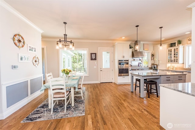 dining area with a chandelier, a wainscoted wall, light wood-style flooring, and crown molding