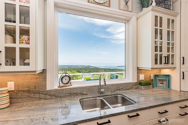 kitchen with a sink, glass insert cabinets, dark stone countertops, and white cabinetry