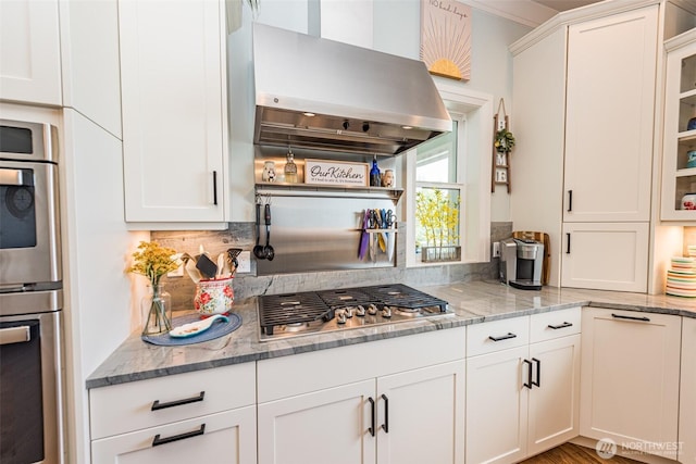 kitchen featuring light stone counters, stainless steel gas stovetop, range hood, and white cabinetry