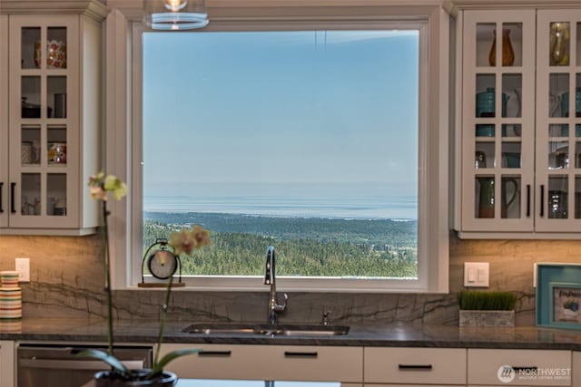 kitchen featuring tasteful backsplash, white cabinetry, glass insert cabinets, and a sink