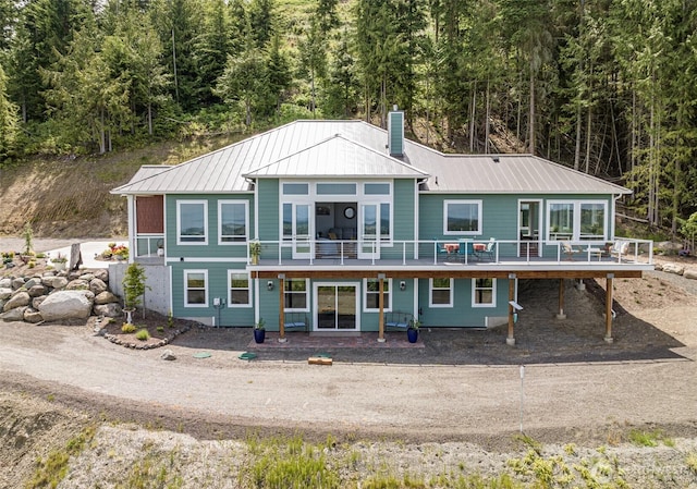 back of house featuring a view of trees, a chimney, a standing seam roof, and metal roof