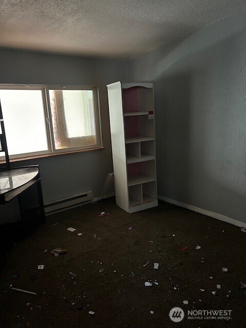 unfurnished bedroom featuring a textured ceiling, a baseboard heating unit, and baseboards