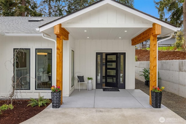 doorway to property featuring board and batten siding, a shingled roof, and fence