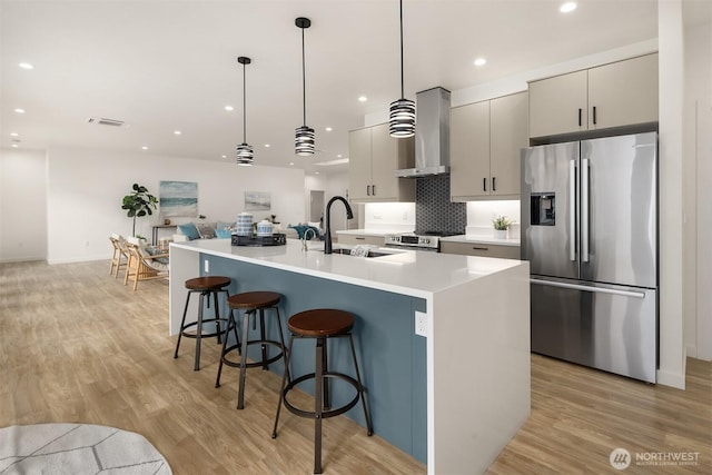 kitchen with a sink, stainless steel appliances, open floor plan, wall chimney exhaust hood, and light wood-type flooring