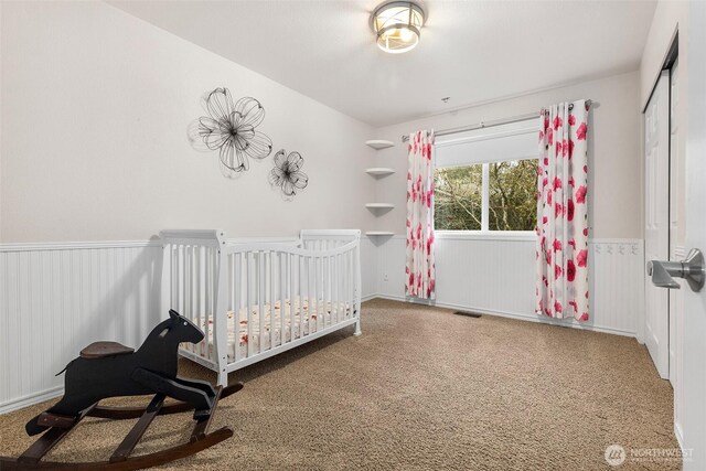 unfurnished bedroom featuring visible vents, wainscoting, a crib, and carpet flooring