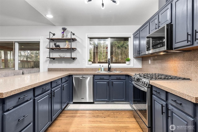 kitchen featuring light wood-style flooring, a sink, a peninsula, appliances with stainless steel finishes, and decorative backsplash