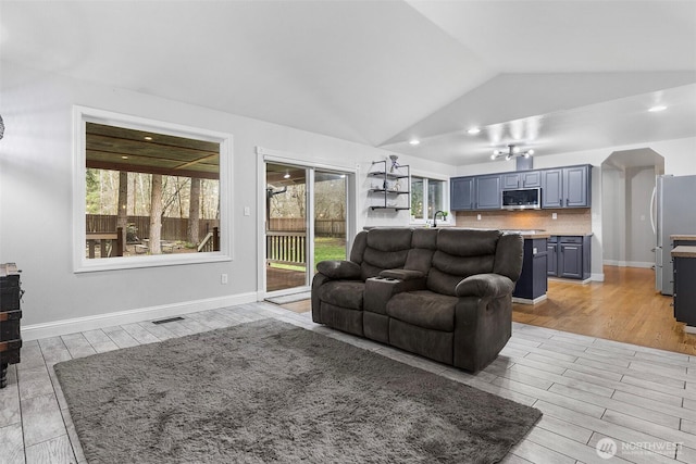 living area featuring visible vents, light wood-style flooring, baseboards, and lofted ceiling