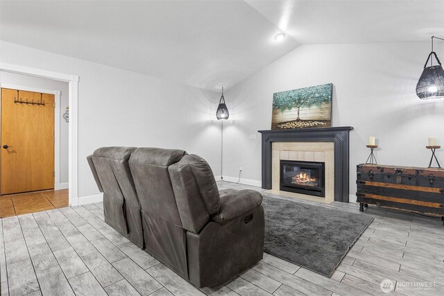 living room featuring a glass covered fireplace, baseboards, wood finish floors, and vaulted ceiling