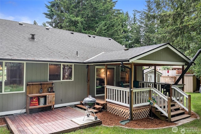 back of house with fence, a wooden deck, roof with shingles, an outbuilding, and a storage unit