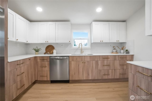 kitchen with light wood finished floors, dishwasher, light countertops, white cabinets, and a sink