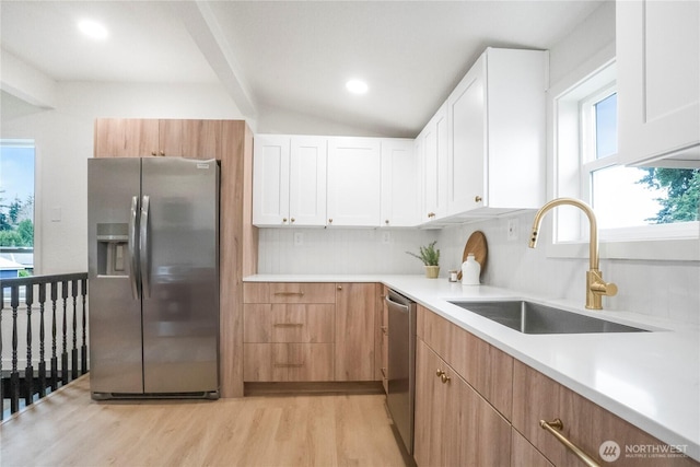 kitchen featuring a sink, appliances with stainless steel finishes, light wood finished floors, light countertops, and vaulted ceiling