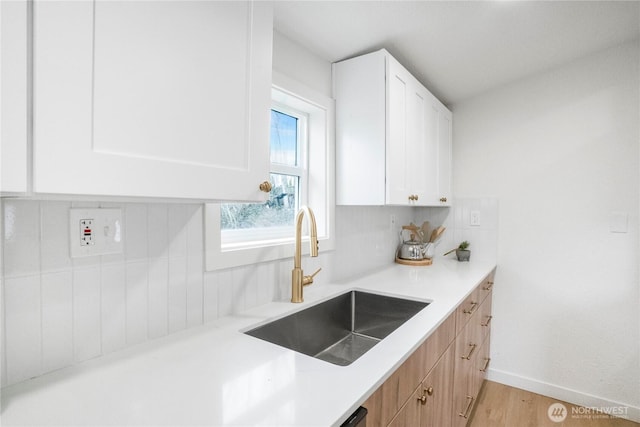 kitchen featuring decorative backsplash, light countertops, white cabinetry, and a sink