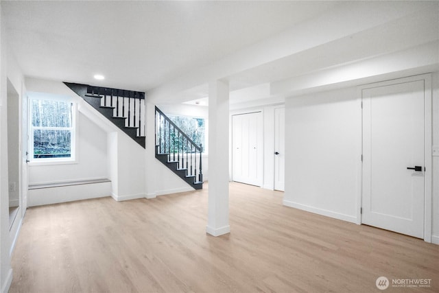 below grade area featuring a baseboard heating unit, baseboards, wood finished floors, and stairs