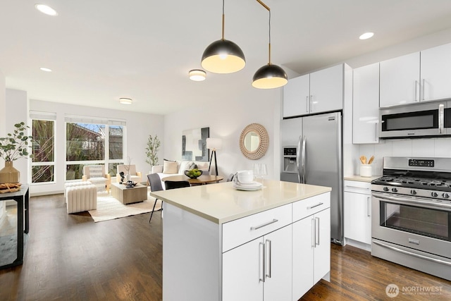 kitchen with dark wood-type flooring, decorative light fixtures, open floor plan, light countertops, and appliances with stainless steel finishes