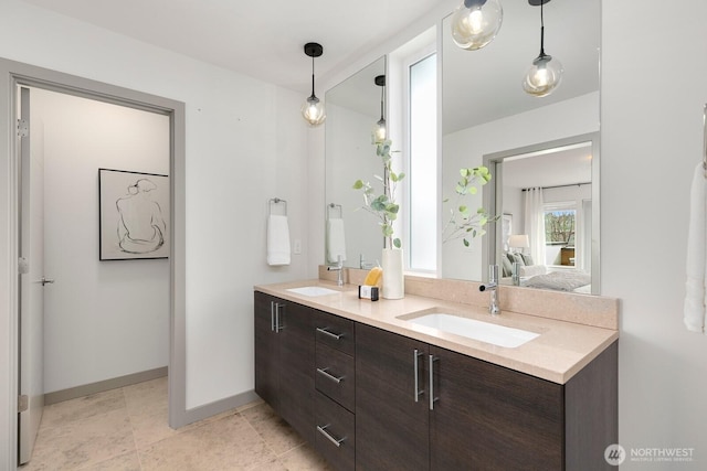 ensuite bathroom with double vanity, connected bathroom, baseboards, and a sink