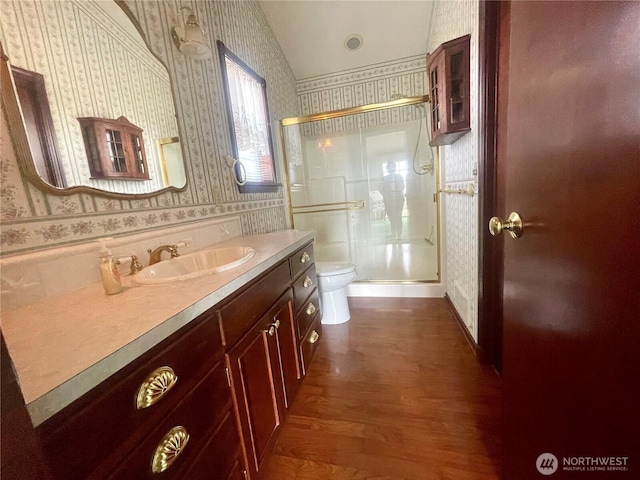 bathroom featuring vanity, wood finished floors, wallpapered walls, a stall shower, and toilet