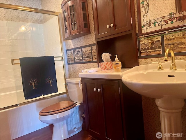 full bathroom featuring wallpapered walls, toilet, shower / bath combination with glass door, and a sink