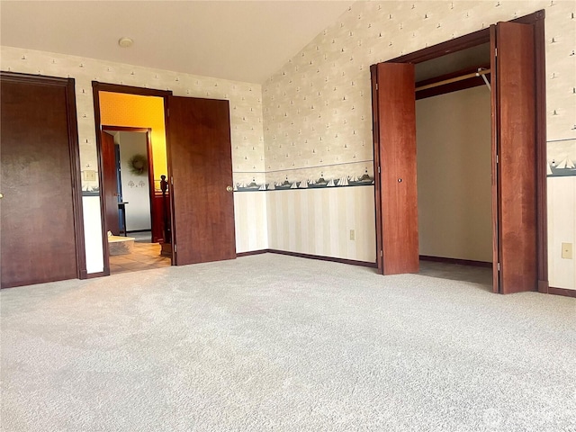 unfurnished bedroom featuring wallpapered walls, lofted ceiling, and carpet