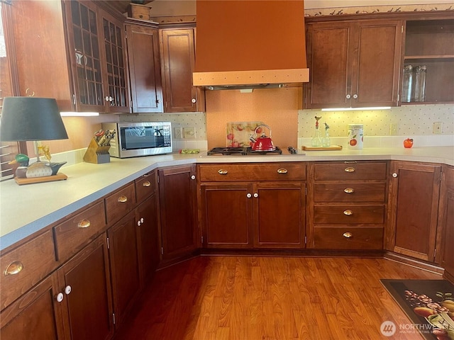 kitchen with stainless steel appliances, wall chimney exhaust hood, light countertops, and wood finished floors