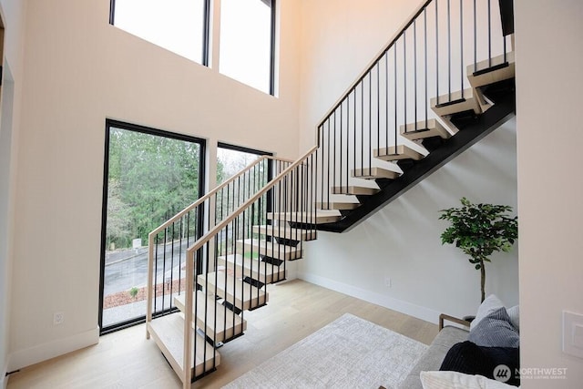 stairs featuring a high ceiling, baseboards, and wood finished floors