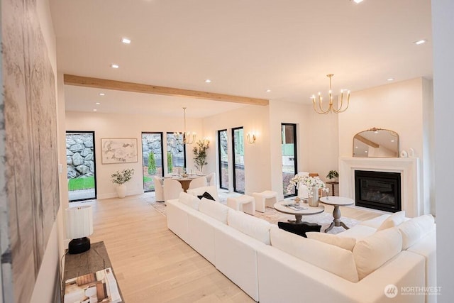 living room with beam ceiling, a notable chandelier, a glass covered fireplace, recessed lighting, and light wood-style floors