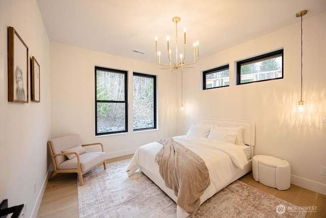 bedroom featuring visible vents, light wood-style flooring, an inviting chandelier, and baseboards