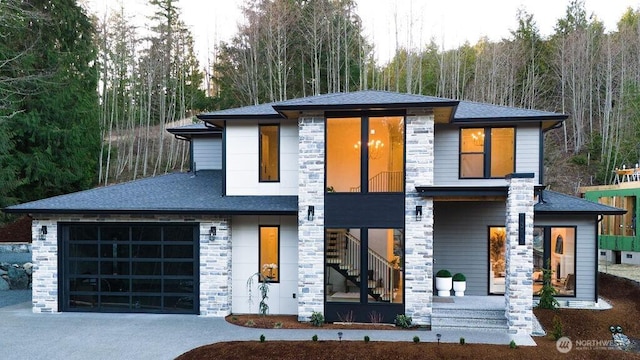 view of front of home with driveway, stone siding, stairway, roof with shingles, and a garage