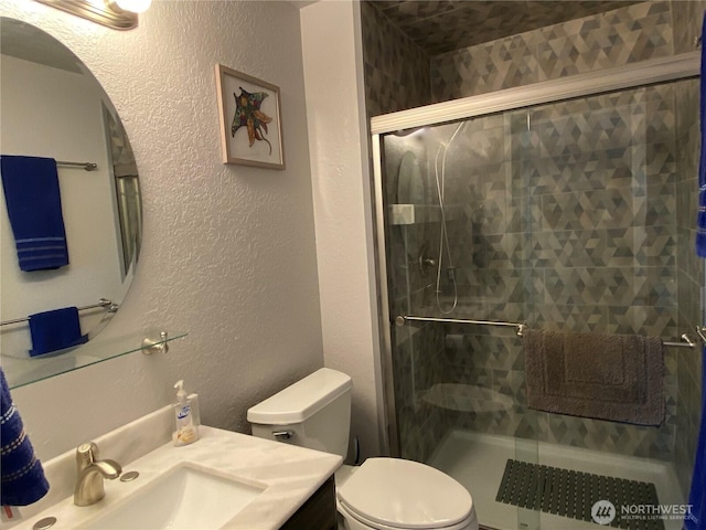 full bathroom with vanity, a shower stall, toilet, and a textured wall