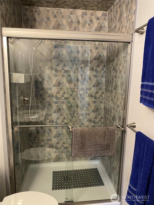 bathroom with a shower stall, toilet, and a textured wall