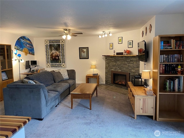 living area featuring carpet flooring, a textured ceiling, a stone fireplace, and a ceiling fan