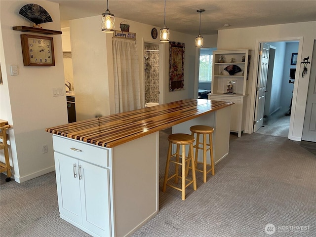 kitchen featuring wooden counters, a kitchen island, light colored carpet, hanging light fixtures, and white cabinetry