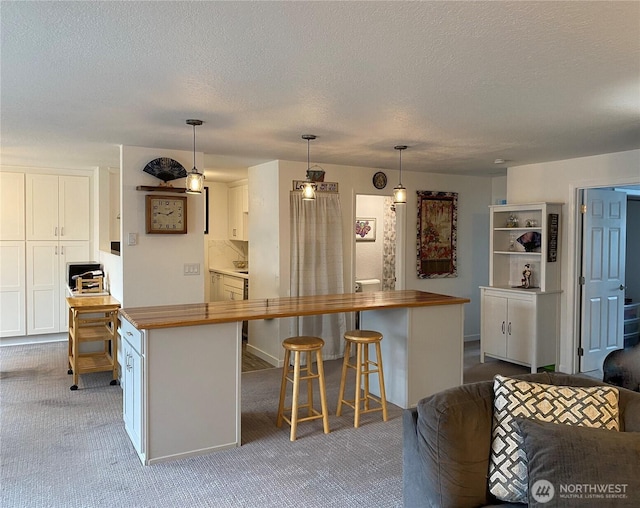 kitchen with a kitchen breakfast bar, white cabinetry, wood counters, and carpet