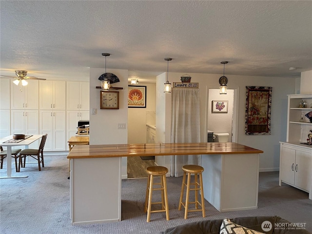 kitchen featuring white cabinetry, hanging light fixtures, dark colored carpet, and wood counters