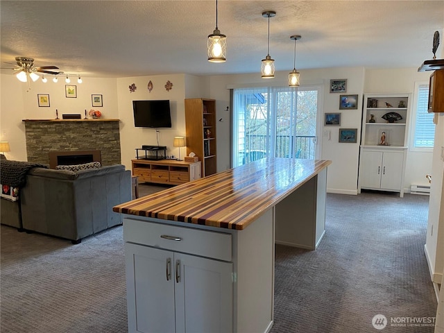 kitchen with wooden counters, a stone fireplace, a textured ceiling, dark colored carpet, and a center island