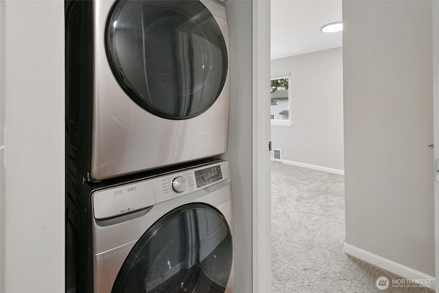 clothes washing area featuring laundry area, stacked washer / dryer, carpet, and baseboards