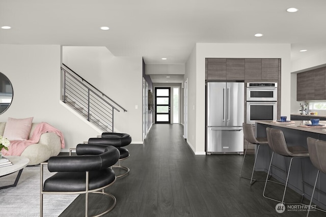 kitchen featuring dark wood-style floors, recessed lighting, stainless steel appliances, a kitchen bar, and modern cabinets