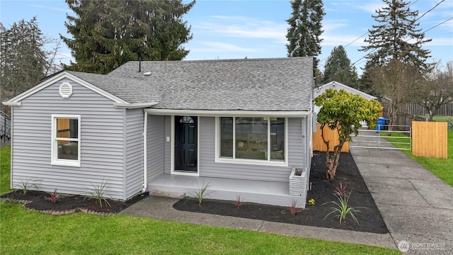 view of front facade with a front yard, fence, and a shingled roof