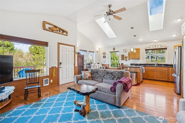 living room with a ceiling fan, a skylight, light wood-style floors, and high vaulted ceiling