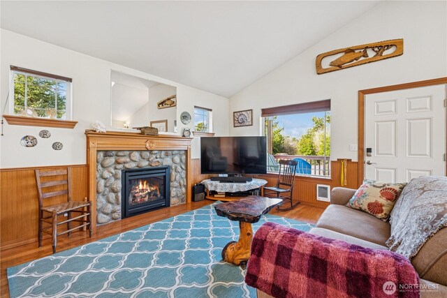 living area with a stone fireplace, plenty of natural light, lofted ceiling, and wainscoting