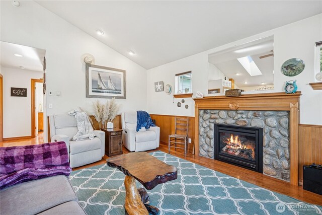 living room with vaulted ceiling with skylight, a fireplace, wood finished floors, and wainscoting