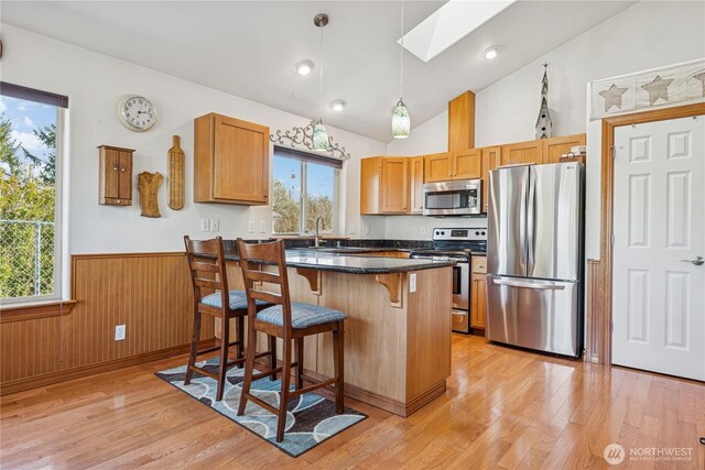 kitchen featuring appliances with stainless steel finishes, a breakfast bar, wainscoting, and light wood finished floors