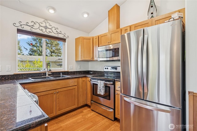 kitchen with a sink, light wood-style floors, appliances with stainless steel finishes, and vaulted ceiling