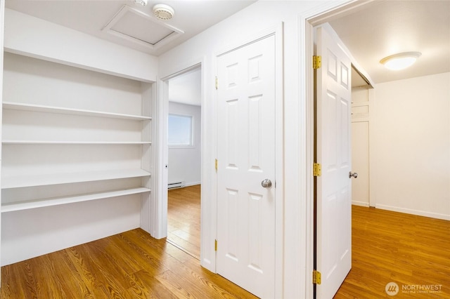 corridor featuring baseboards, baseboard heating, attic access, and wood finished floors