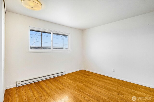 empty room with baseboard heating, baseboards, and wood finished floors